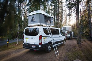 a van is parked in the woods with a tent on top.