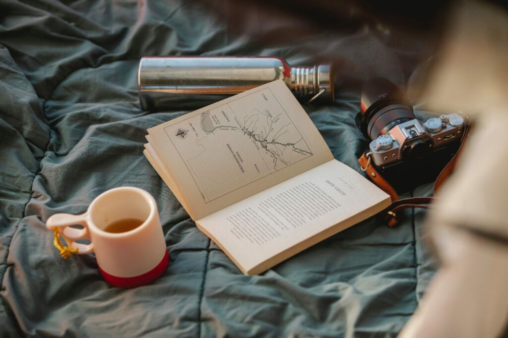 A woman is sitting on a bed with a book and a cup of coffee.